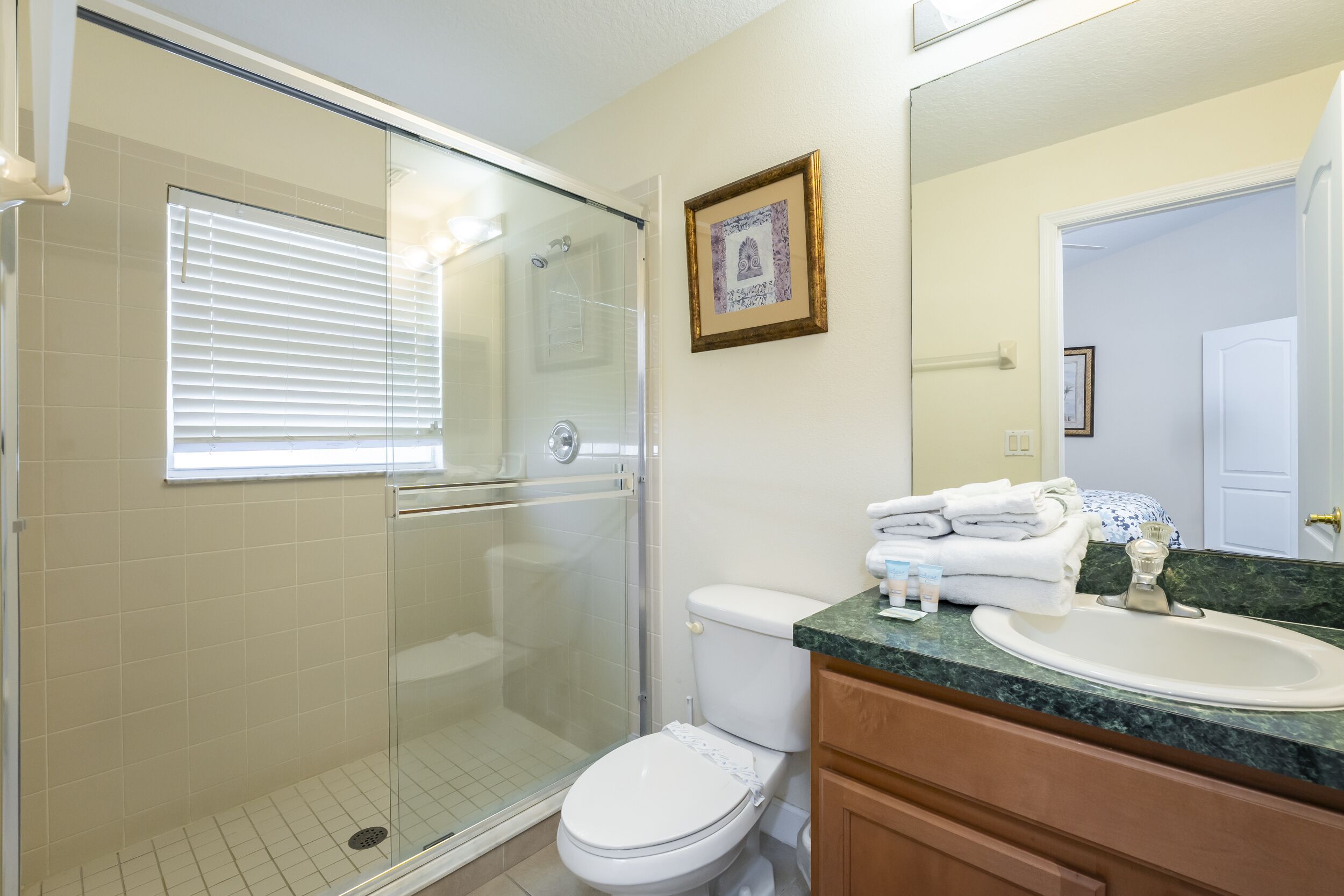 Une salle de bain avec une douche à parois de verre, des toilettes, un lavabo doté d’un plan de travail en marbre et un tableau encadré au mur.