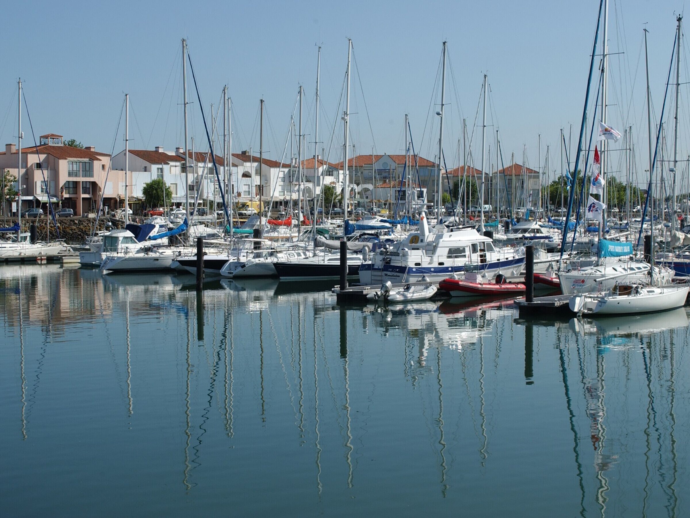 A marina with multiple boats docked, surrounded by buildings with red-tiled roofs.