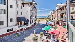 A cobblestone street with outdoor seating and umbrellas, a building with a sign reading "The Pearl", and a view of the ocean. - Gulf View: Crown Studio on Main St, across from Pearl Hotel (Rosemary Beach)