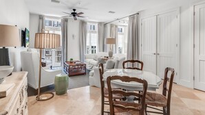 A spacious living room with a ceiling fan, a dining area with a round table and chairs, and a large window with curtains. - Gulf View: Crown Studio on Main St, across from Pearl Hotel (Rosemary Beach)