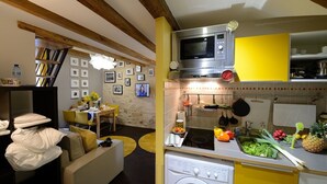 Cocina compacta con microondas, estufa y lavadora. Hay una zona de comedor con mesa y sillas, y un sofá con cojines.