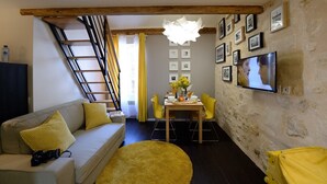 Una sala de estar acogedora con un sofá, una mesa de comedor con sillas, un televisor montado en la pared y una escalera.