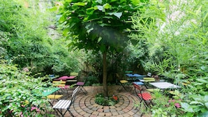 Un patio circular de ladrillo con mobiliario exterior colorido y un árbol en el centro.