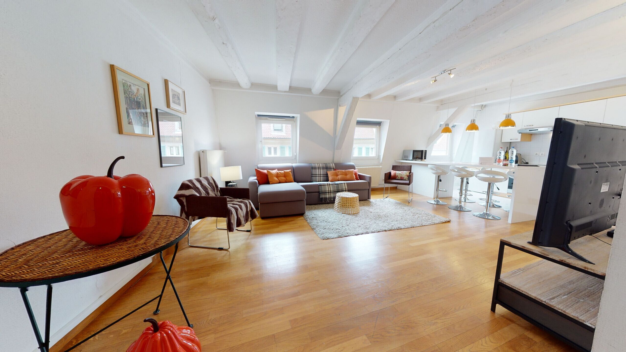 A spacious living area with a sofa, a coffee table, and a TV. There are multiple windows providing natural light.