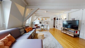 A modern living room with a sofa, a TV, and a kitchen in the background.