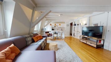 A modern living room with a sofa, a TV, and a kitchen in the background.