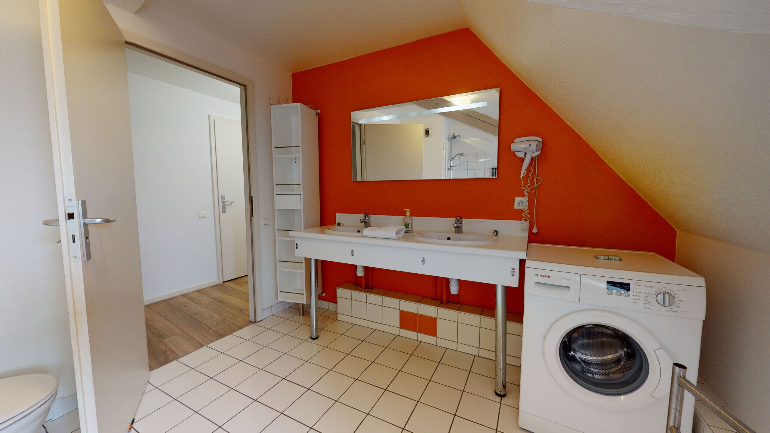 Een kleine, lichte badkamer met een witte wastafel, een spiegel en een Bosch wasmachine.