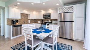 Una cocina moderna con armarios blancos, electrodomésticos de acero inoxidable y un mantel individual azul sobre la mesa de comedor.