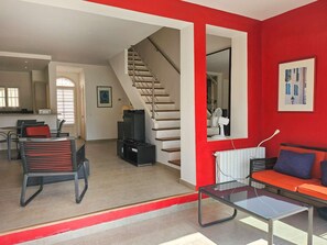 Un salon avec un mur d’accent rouge, un escalier, un canapé, une table basse et un téléviseur.