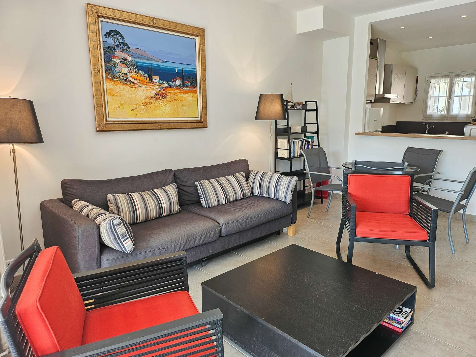 A modern living room with a grey sofa, striped pillows, a black coffee table, and a red chair.