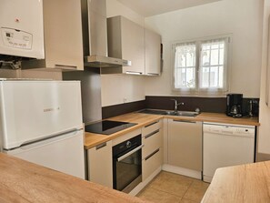 A compact kitchen with a refrigerator, stove, oven, dishwasher, and a window with curtains. - Lovely House for 4 persons  et  10.50 m mooring (PORT GRIMAUD)