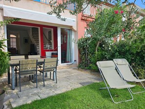 Une terrasse avec une table et des chaises, un fauteuil de relaxation et un jardin agrémenté d’une clôture et de plantes.