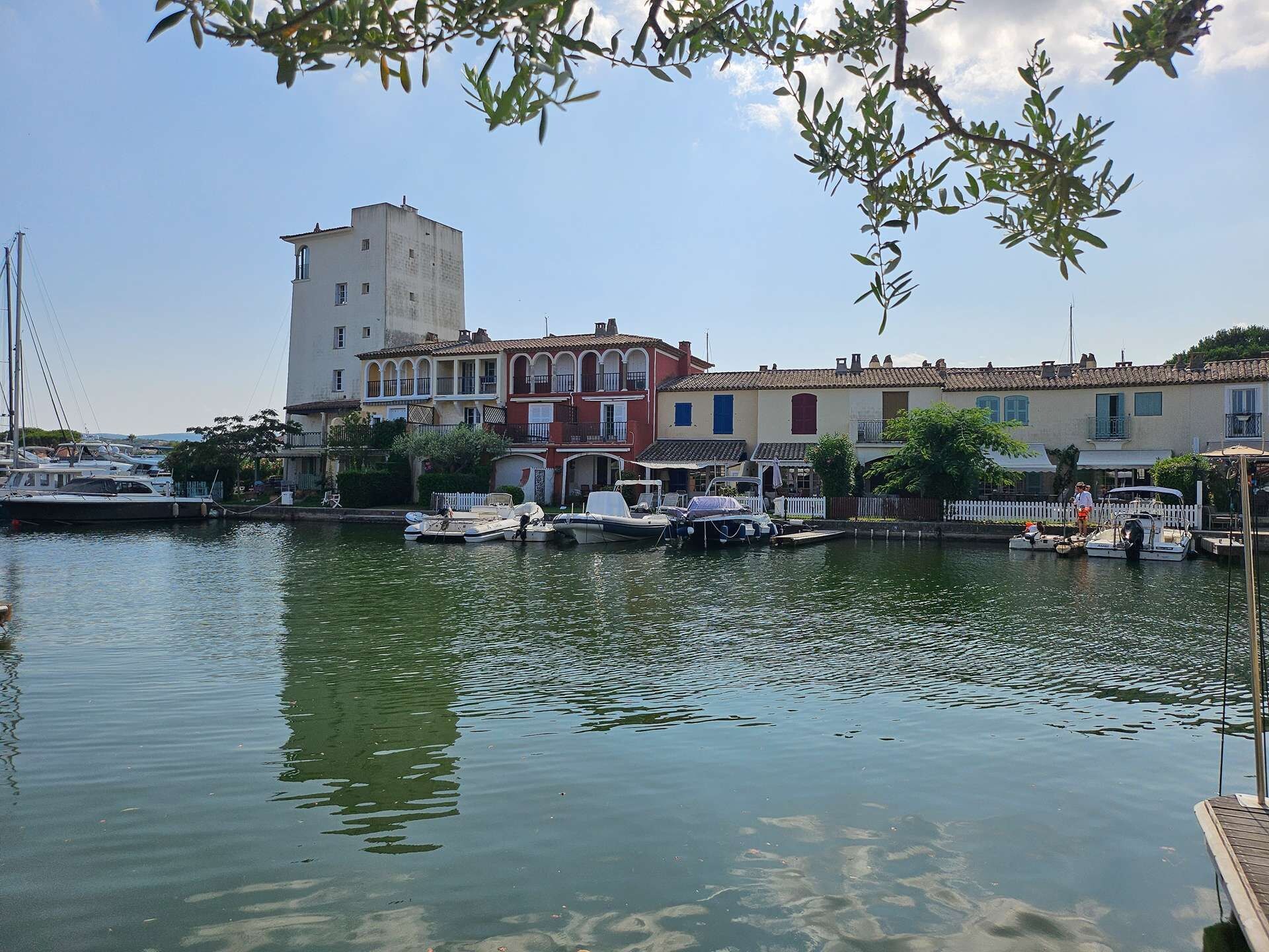 A marina with boats docked, a tower building, and colorful houses along the waterfront.