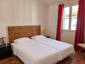 Un lit double avec une tête de lit en bois, dans une chambre dotée d’une fenêtre et de rideaux rouges.
