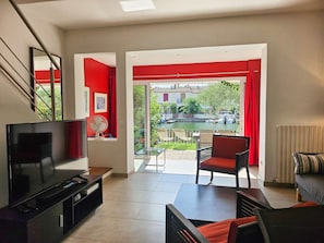 A modern living room with a TV, seating, and a view of a courtyard with a boat. - Lovely House for 4 persons  et  10.50 m mooring (PORT GRIMAUD)