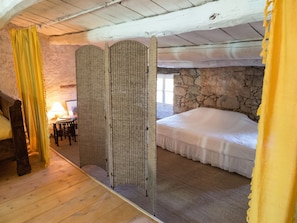 A bedroom with a stone wall, a bed, a wooden floor, and a yellow curtain.
