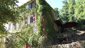 A rustic stone building with ivy-covered walls and red shutters, featuring a stone staircase and a metal railing. - Homerez - Flat in Feliceto (Feliceto)