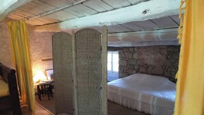 A bedroom with a stone wall, a bed, a wooden floor, and a window. - Homerez - Flat in Feliceto (Feliceto)