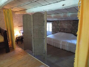 Une chambre avec un mur en pierre, un lit, un plancher en bois et une fenêtre.