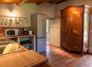 A kitchen with a microwave, coffee maker, and refrigerator. There is a wooden cabinet and a tiled floor.