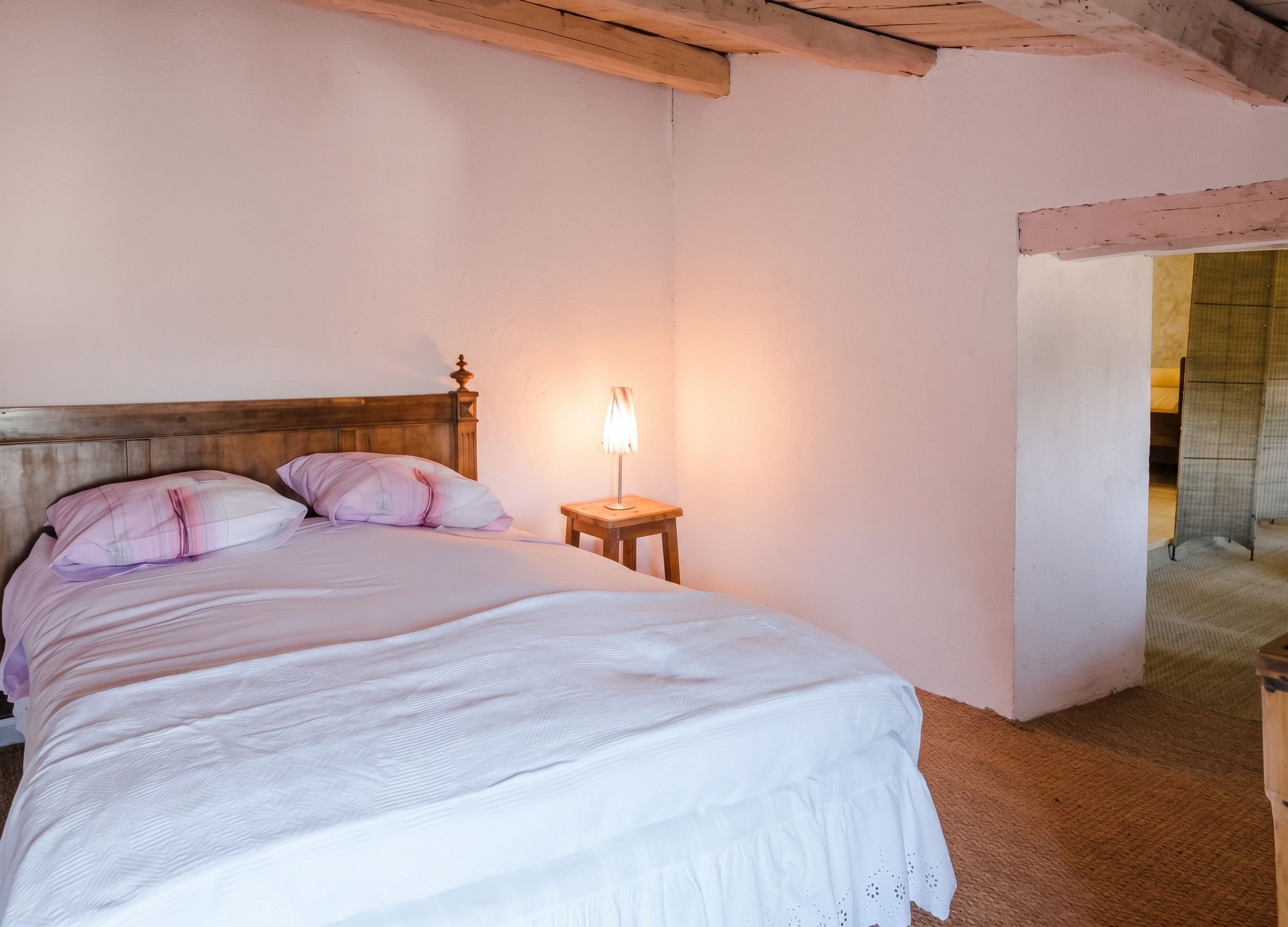 A bedroom with a wooden headboard, a bedside lamp, and a bed with white bedding.