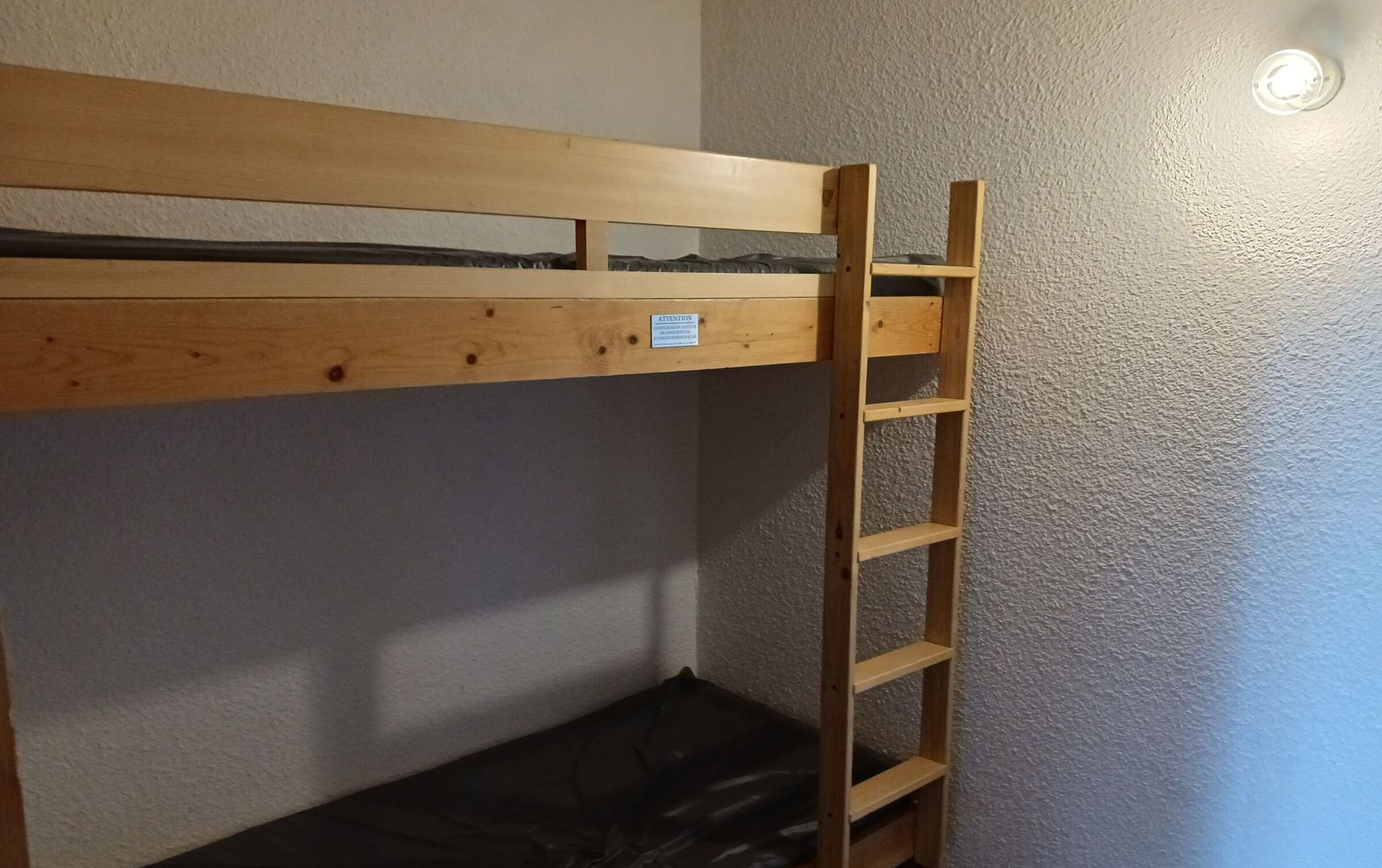 A bunk bed with a wooden ladder and a small shelf.