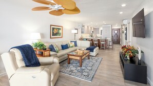 Ein geräumiges Wohnzimmer mit Deckenventilator, einer Couch, einem Couchtisch und einer Küche im Hintergrund.