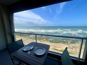 A balcony with a table set for two, overlooking a rocky shoreline and the ocean. - Studio with balcony, WIFI, and parking near the beach (Les Sables-d'Olonne)