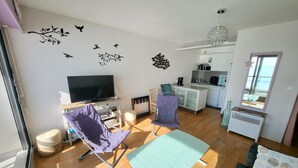 A compact living space with a TV, seating area, kitchenette, and a view of the outdoors. - Studio with balcony, WIFI, and parking near the beach (Les Sables-d'Olonne)