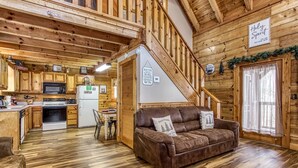 Ein gemütliches Blockhaushaus-Interieur mit Küche, Essbereich und einer Treppe, die zu einem Schlafbereich im Obergeschoss führt.