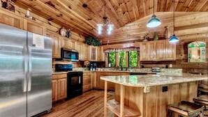 A wooden cabin-style kitchen with a large island, stainless steel refrigerator, and wooden cabinets. - Secluded, Close to Town, Hot Tub, Fire Pit, WiFi, Pets Ok! (Fairview)