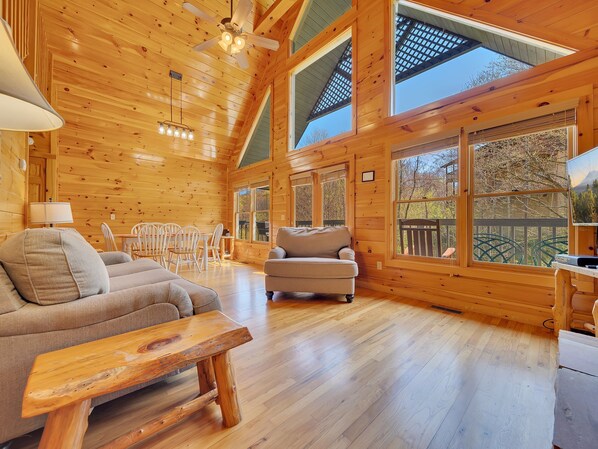 Cozy cabin interior with a high ceiling and exposed beams, featuring a dining table, sofa, and wooden bench.