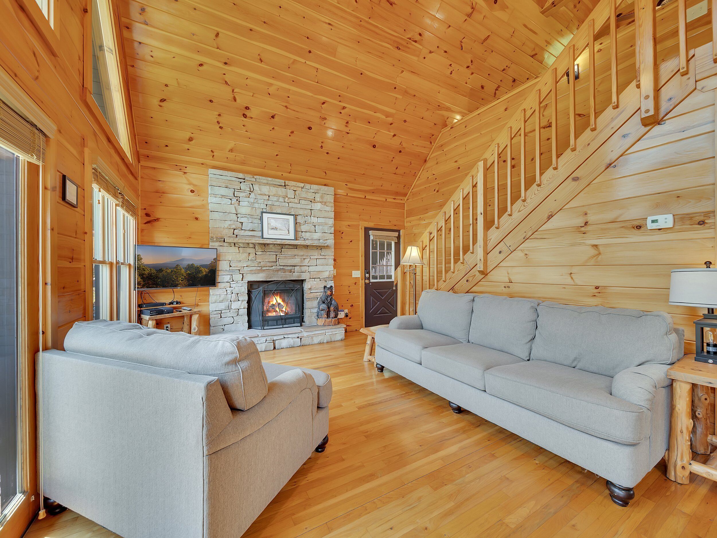 Ein gemütliches Blockhaus-Interieur mit Kamin aus Stein, Holzböden, einer Couch und einer Treppe.