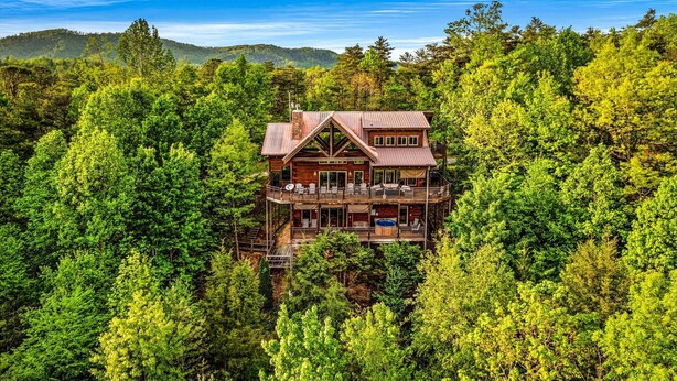 Una baita di legno a due piani con un balcone, immersa in una fitta foresta.