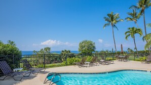 A pool area with lounge chairs, a small table, and a view of the ocean. - Ocean view, Country Club Villas 224, No stairs, 2nd floor unit. (Kailua-Kona)