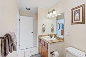 A bathroom with a white toilet, a sink with a granite countertop, a mirror above the sink, and a towel rack with towels. - Ocean view, Country Club Villas 224, No stairs, 2nd floor unit. (Kailua-Kona)