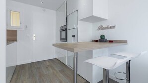 A modern kitchen with white cabinetry, a wooden countertop, and a bar area with two white bar stools. - Haven of Peace: 1-Br Terrace with Sea View & Pool (Cannes)