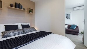 A modern bedroom with a large bed, a wooden headboard, and built-in shelves with decorative items. - Haven of Peace: 1-Br Terrace with Sea View & Pool (Cannes)