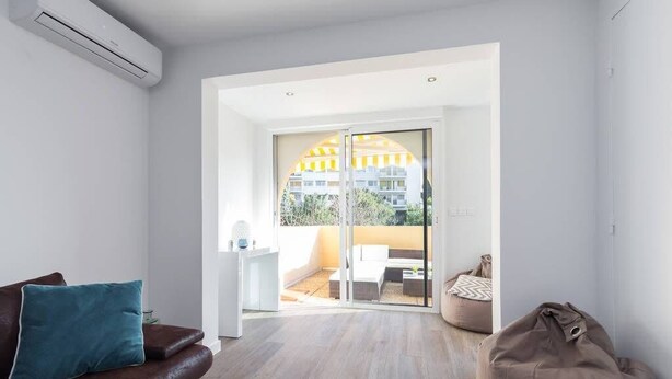 A modern living room with a brown leather sofa, a beige bean bag, and a glass door leading to a balcony with a yellow railing. - Haven of Peace: 1-Br Terrace with Sea View & Pool (Cannes)