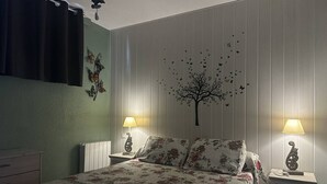 A bedroom with a bed, two bedside tables with lamps, a dresser, and a wall with a tree decal and butterflies.