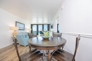 A dining area with a round table, four chairs, a sofa, and a vase with flowers.