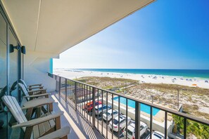A balcony with chairs, a pool, and a view of the beach.