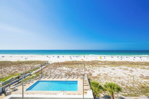 A pool with lounge chairs, a beach with umbrellas, and a clear blue sky.