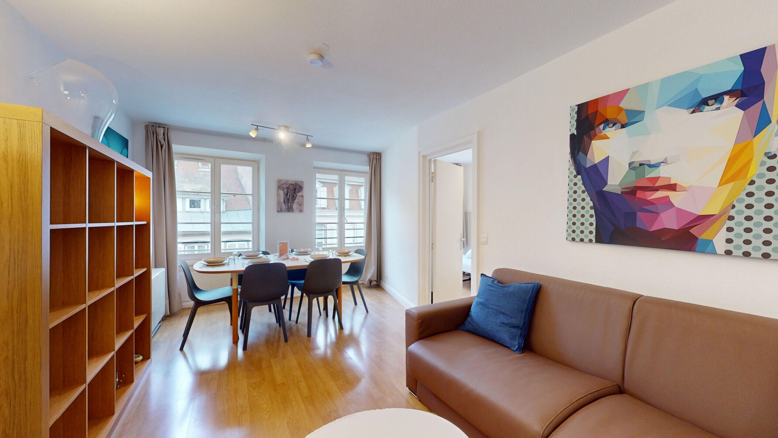 Een moderne woonkamer met een bruine leren bank, een eethoek met een tafel en stoelen, en een groot abstract schilderij aan de muur.