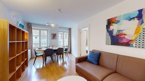 A modern living room with a brown leather sofa, a dining area with a table and chairs, and a large abstract painting on the wall.