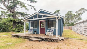 Une petite maison bleue avec un porche, deux fauteuils à bascule et une porte rouge.