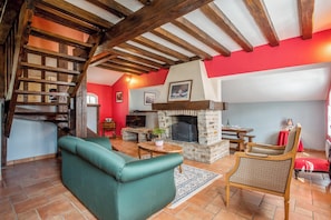 A cozy living room with a stone fireplace, wooden beams, a green sofa, and a dining area. - Homerez - House in Bangor (Bangor)