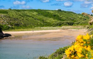 A coastal landscape with a sandy beach, calm water, and green hills in the background. - Homerez - House in Bangor (Bangor)