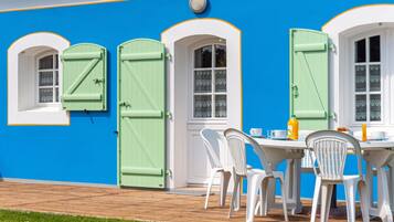 A building with a blue exterior, white trim, and green shutters. There is a table with chairs and a bottle of orange juice.