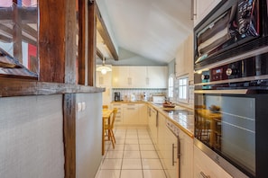 A kitchen with wooden cabinets, a large oven, and a dining area with a table and chairs. - Homerez - House in Bangor (Bangor)
